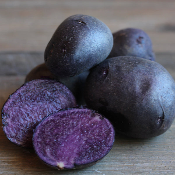 Purple potatoes on a wooden surface with one cut open