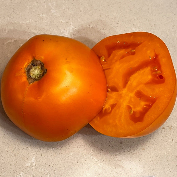 Orange tomato and its half on a beige surface with a blue label.